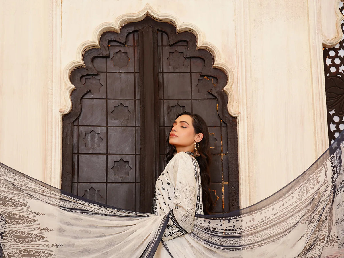 Woman in a white embroidered suit with a printed dupatta at a carved arched door