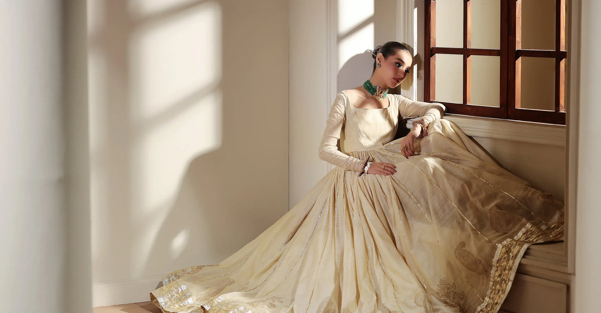 Woman in an ivory and gold formal dress seated by a window